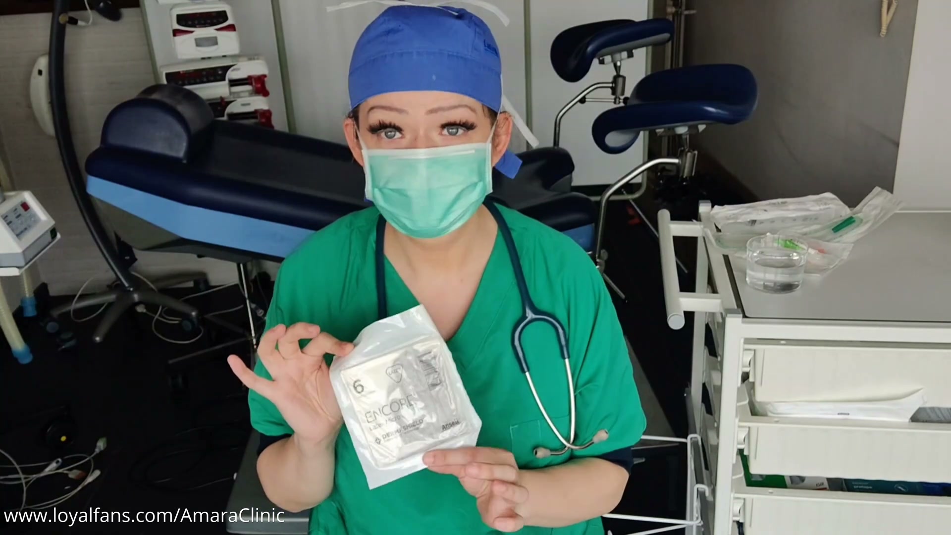Dr. Amara holding a box of Biogel surgical gloves before a gastrointestinal tube medical femdom video and free medical BDSM feeding tube roleplay at Amara Fetish Clinic Belgium