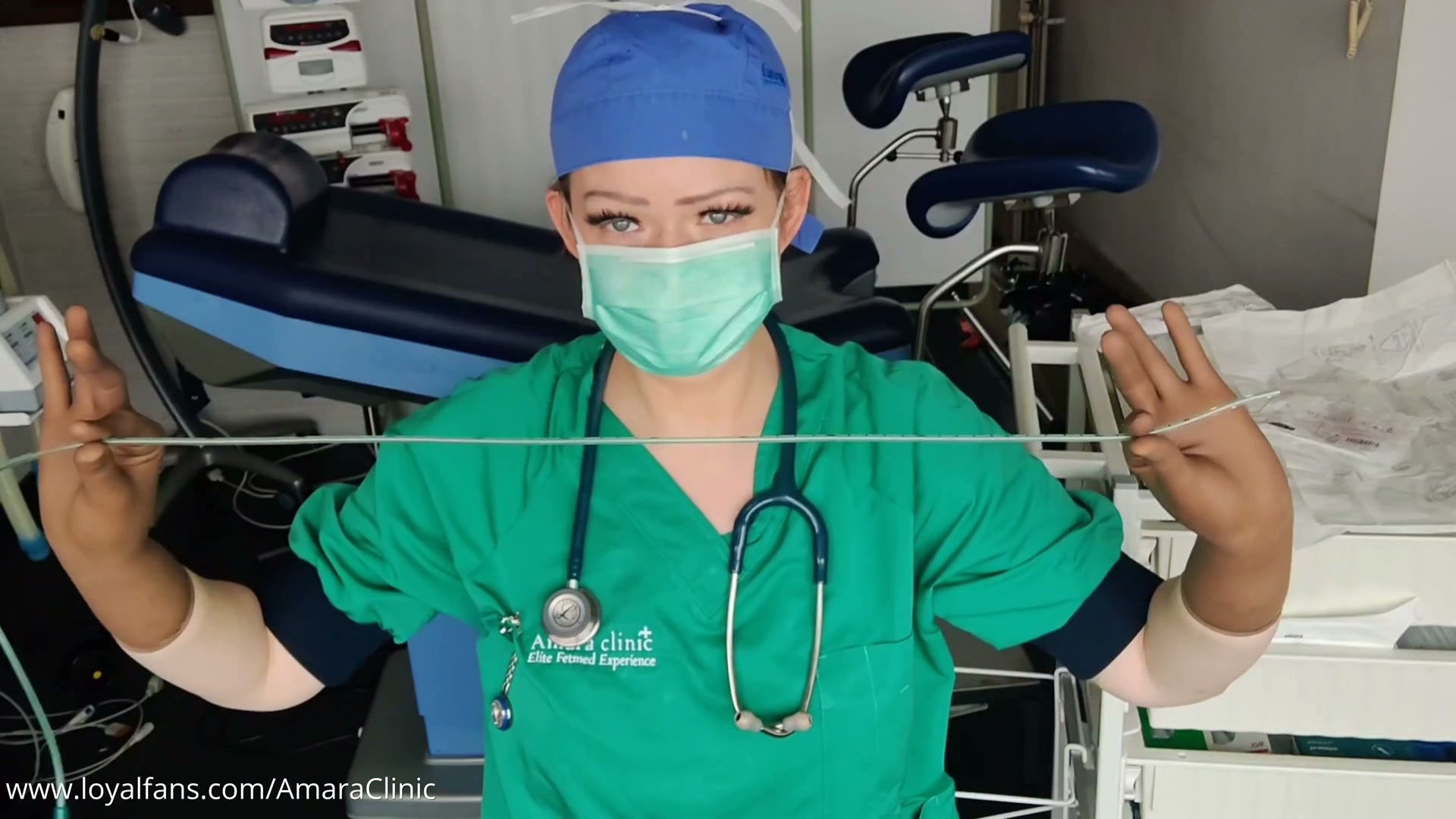 Dr. Amara holding a clear gastrointestinal tube stretched between her gloved hands in a free Dr. Amara gastrointestinal tube medical BDSM video and feeding tube medfet video at Amara Fetish Clinic Belgium