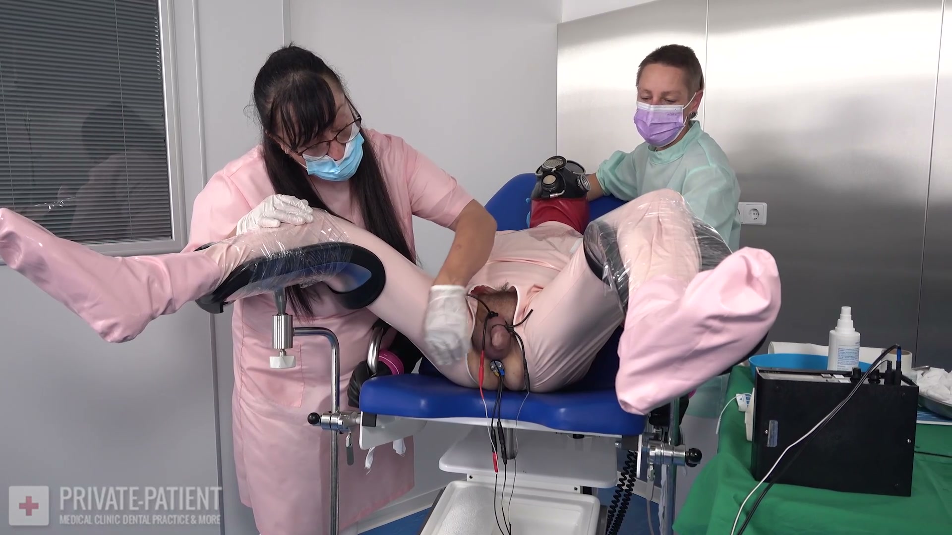 Dr. Ira commanding and Dr. Fuchs submitting over a restrained private patient in the sixth part of the Visitor From France private-patient series, a free Dr. Ira dominant Dr. Fuchs submissive private patient medical BDSM video from Amara Fetish Clinic Belgium